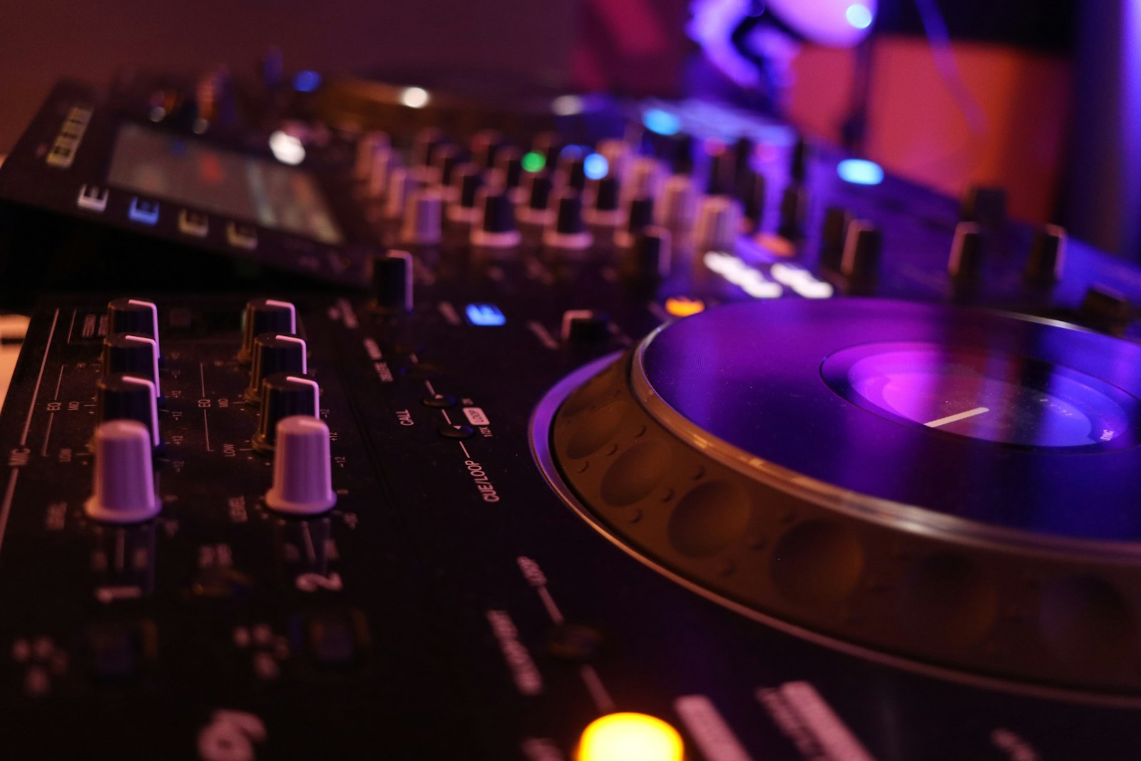 Close-up van een dj-mixer en jog-wheel in amberkleurig licht.